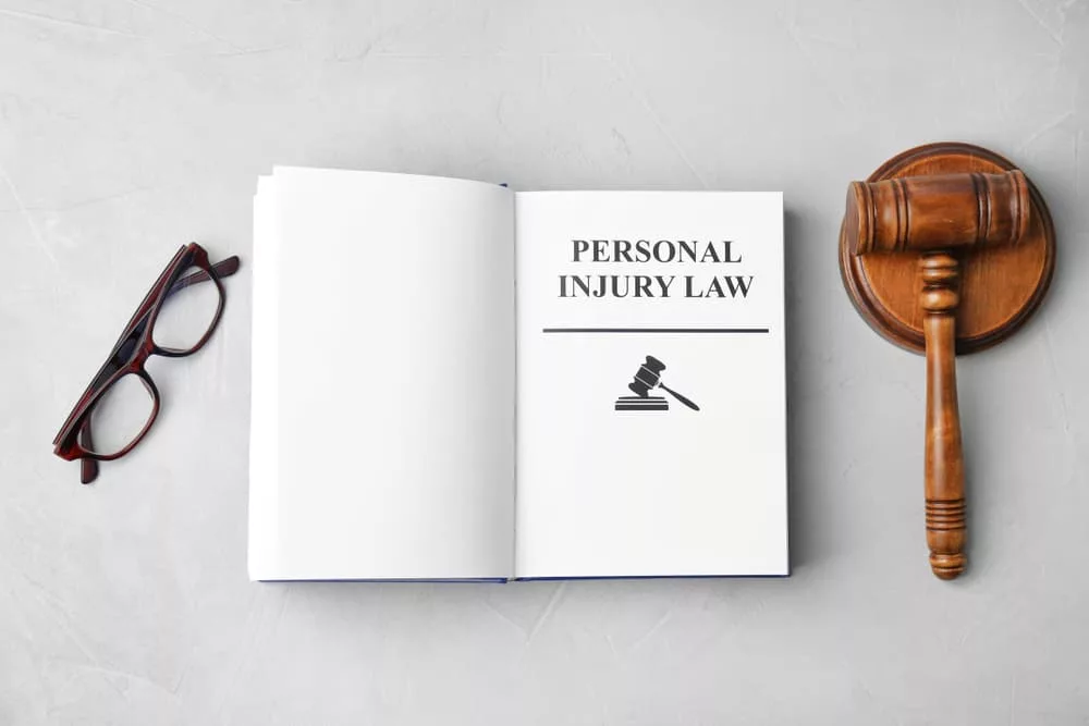 Top view of a grey background with a book titled PERSONAL INJURY LAW accompanied by a gavel and glasses.