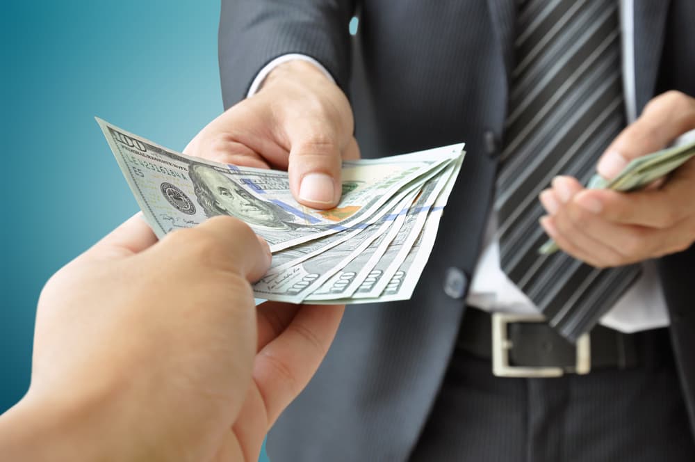Close-up of a hand accepting USD bills from a businessperson in a financial transaction