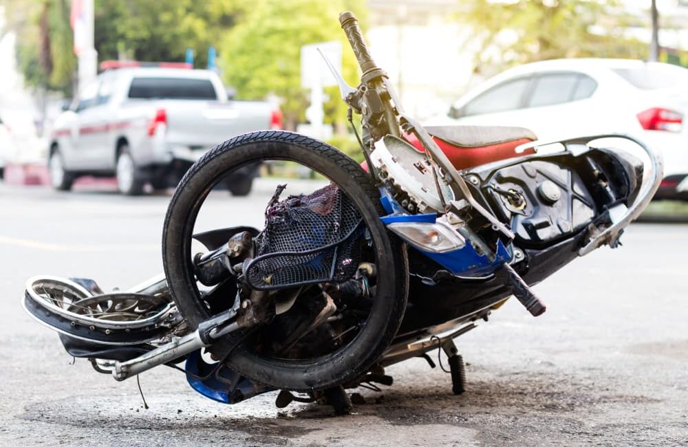 A severely damaged motorcycle after a serious accident, positioned on a paved road near a fence in Miami, FL.
