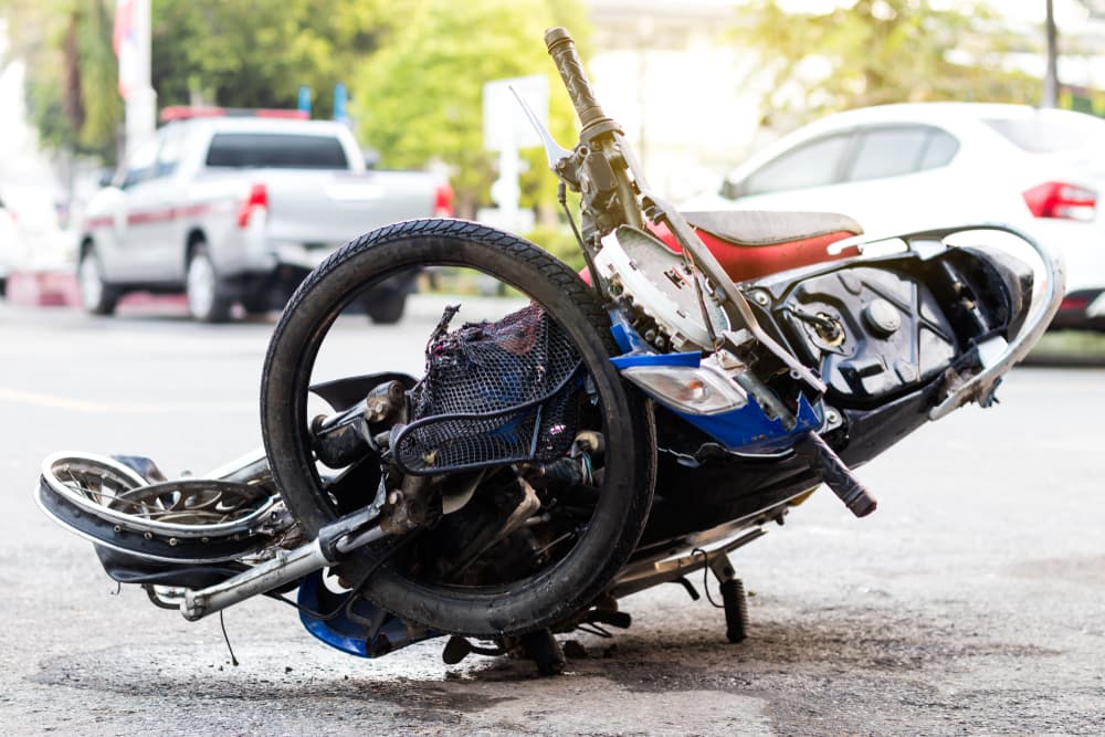 A severely damaged motorcycle after a serious accident, positioned on a paved road near a fence in Miami.