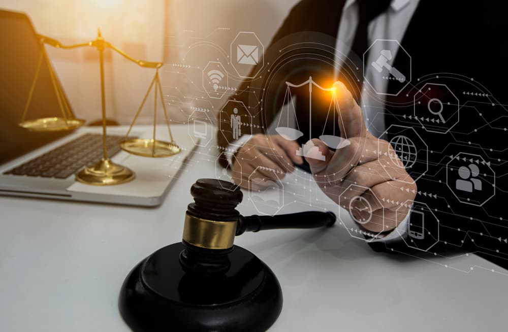A lawyer's hands actively operating a laptop on a modern office table, surrounded by icons representing virtual interfaces related to law innovation.