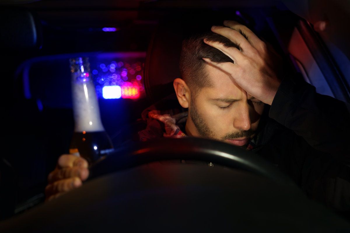 Road police with flashing lights stopped drunk driver. Young man drinking beer while driving car. Driver under alcohol influence